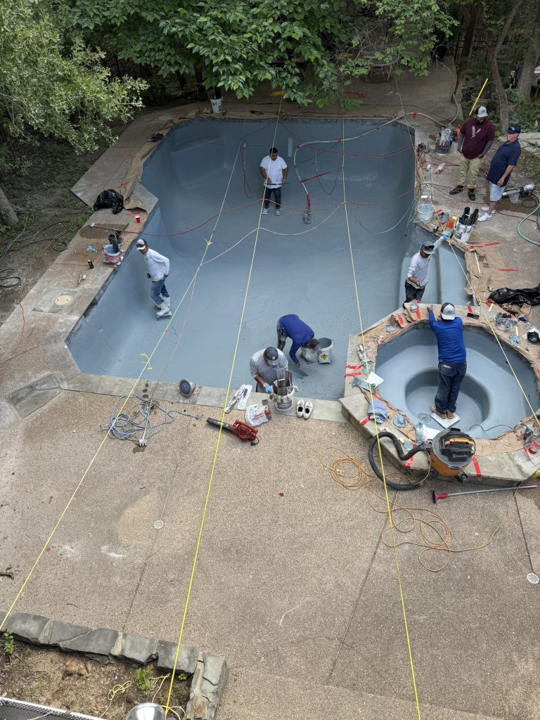 Workers applying a fresh coat of resurfacing material to a pool and spa, surrounded by tools and equipment.