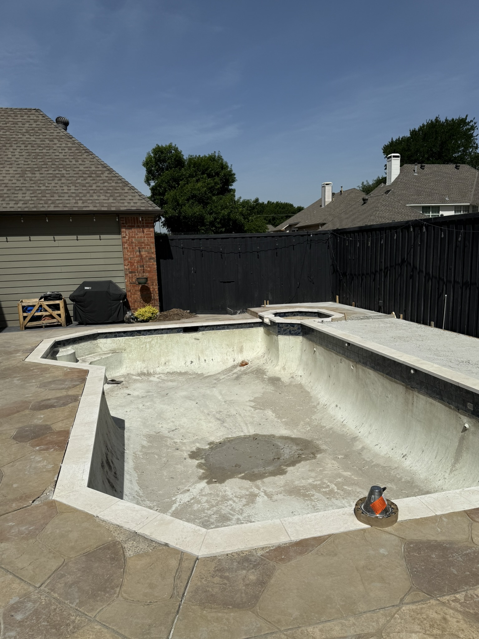 Partially renovated swimming pool showing bare concrete and new tile coping, surrounded by a patio area.