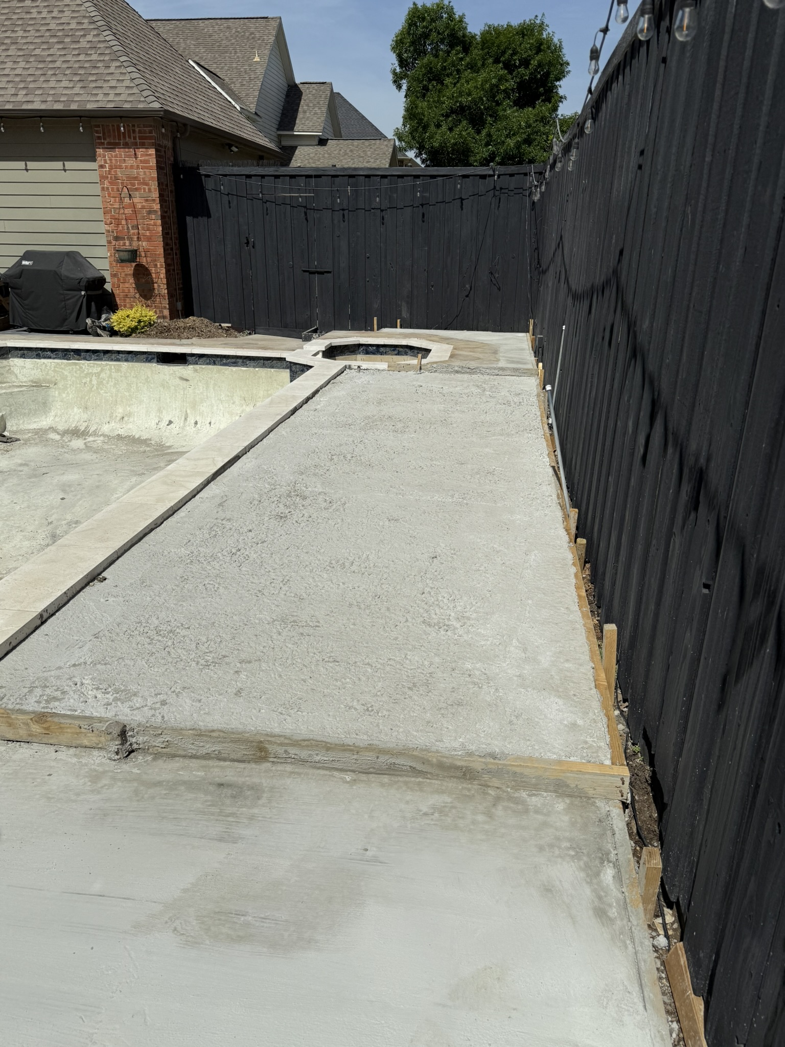 Concrete foundation for a pool remodel, showcasing a partially completed surface with wooden framing and a black fence in the background.