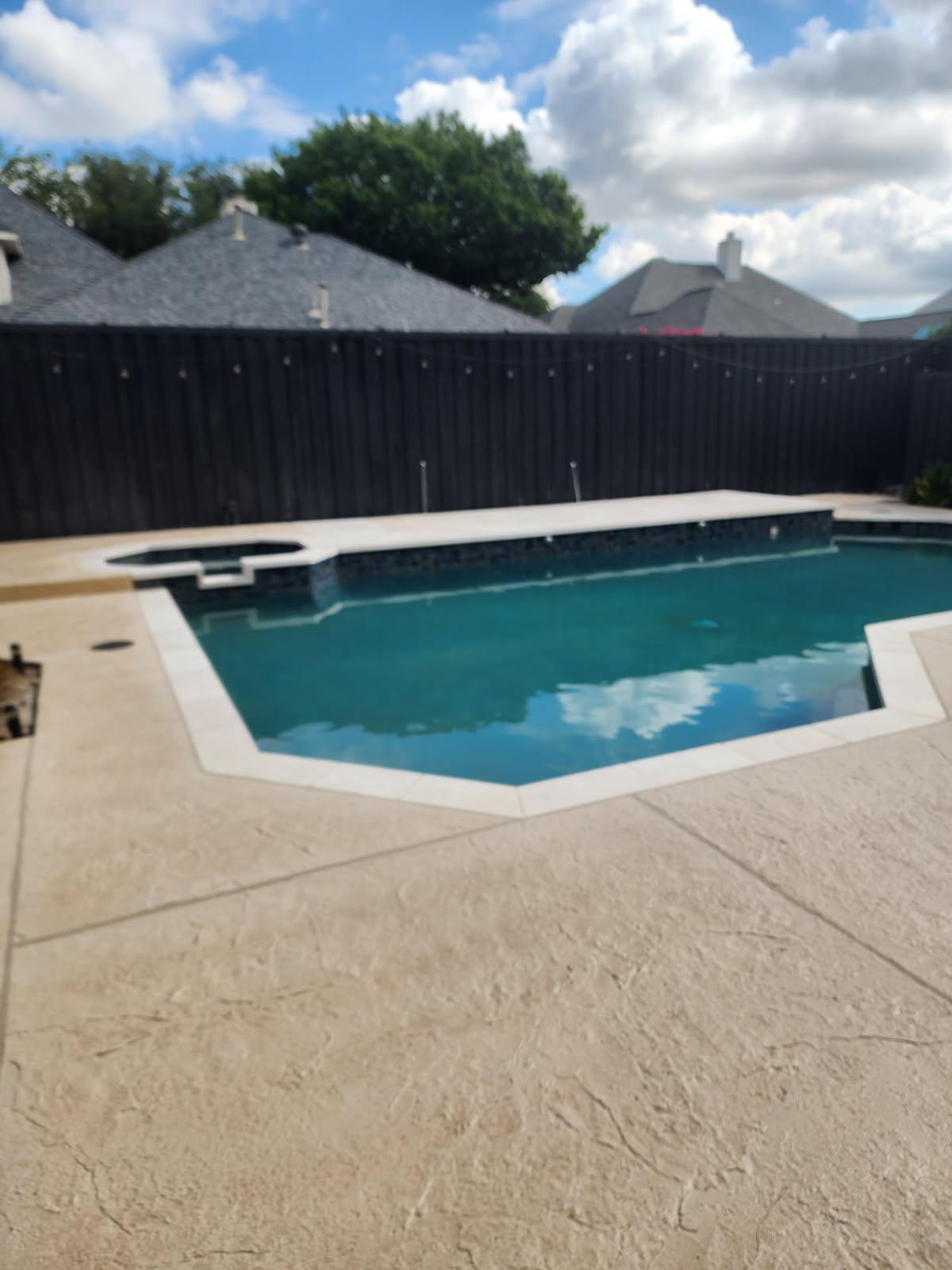 Modern pool with a rectangular design and an attached spa, surrounded by a textured concrete deck and wooden fencing in a residential backyard.
