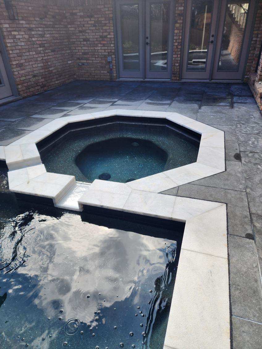 Close-up view of a remodeled pool area featuring an octagonal spa and modern stone coping, with a reflection of the sky on the water's surface.
